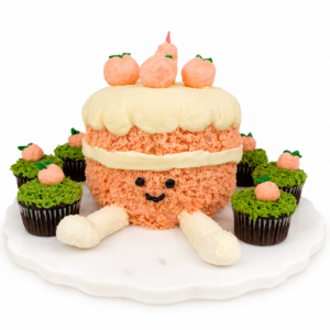 Smiling peach-colored cake with green-frosted garden cupcakes and tiny peach decorations on a clean white background.